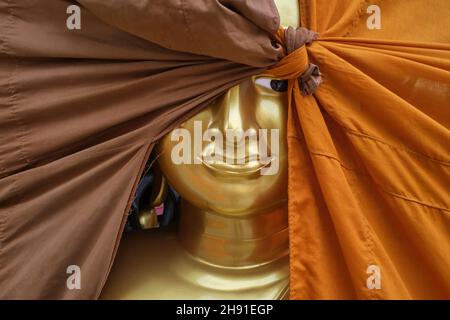 Buddha-Statue in einer Fabrik für buddhistische Objekte in Bamrung Muang Rd., Bangkok, Thailand, ein Auge, das hinter einem orangefarbenen und braunen Stoffbezug herausgucken kann Stockfoto