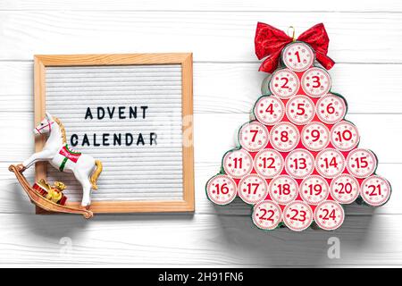 Filztafel, Adventskalender in Form eines Weihnachtsbaums mit Zahlen und Band statt Stern auf weißem Holztisch Weihnachtsadventkalender Concept Top Stockfoto