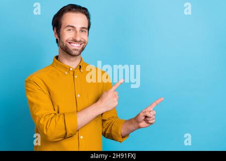 Foto von fröhlichen Promoter Kerl zeigen Finger leeren Raum Neuheit tragen gelbe Hemd isoliert blaue Farbe Hintergrund Stockfoto