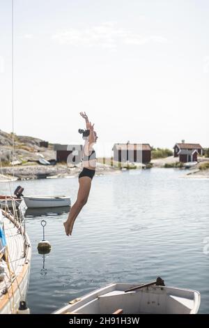 Frau, die während der Sommerferien mit dem Segelboot im Meer springt Stockfoto