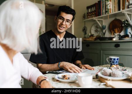Lächelnder männlicher Betreuer, der mit einer älteren Frau in der Küche zu Hause spricht Stockfoto