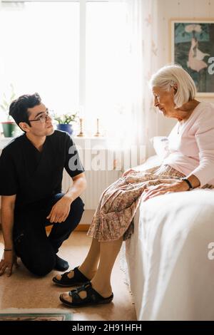 Ältere Frau, die im Schlafzimmer zu Hause mit einem jungen männlichen Gesundheitshelfer spricht Stockfoto