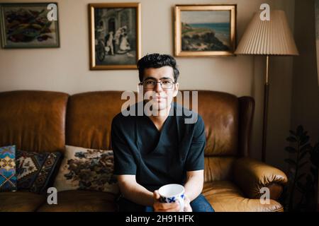 Porträt eines jungen Krankenpflegers mit Kaffeetasse im Wohnzimmer Stockfoto