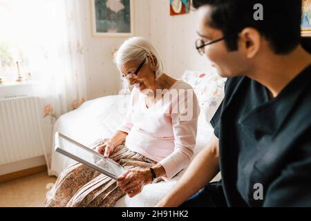 Ältere Frau, die im Spiegel sitzt, während sie im Schlafzimmer beim männlichen Betreuer sitzt Stockfoto