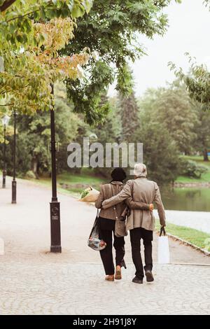 Rückansicht eines älteren Paares, das mit den Armen auf einem Fußweg im Park herumläuft Stockfoto