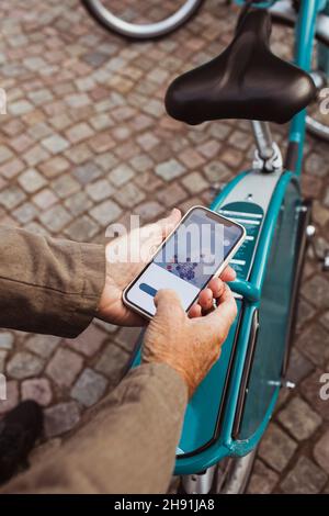 Verkürzte Hände eines älteren Mannes, der den QR-Code des Fahrrads scannt, während er über das Smartphone an der Parkstation telefoniert Stockfoto