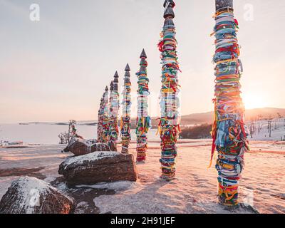 Traditionelle buryat Schamanen-Säulen mit bunten Bändern im Winter bei Sonnenuntergang, Kap Burkhan, Olkhon Insel. Winter Baikal. Stockfoto