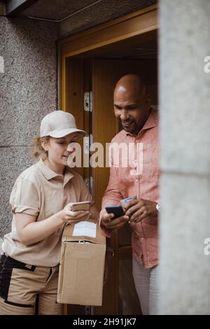 Junge gebliebene Frau und männlicher Kunde, die Smartphones vor der Tür benutzen Stockfoto