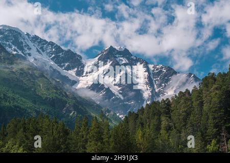 Schneebedeckte Berggipfel an sonnigen Sommertagen mit blauem Himmel und Wolken im Hintergrund, grünes Gras davor. Schöne Landschaft der Kaukasus-Berge. Stockfoto