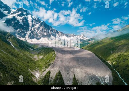 Schneebedeckte Berggipfel an sonnigen Sommertagen mit blauem Himmel und Wolken im Hintergrund, grünes Gras davor. Schöne Landschaft der Kaukasus-Berge. Stockfoto