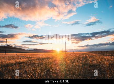 Atemberaubende ländliche Landschaft. Sonnenuntergang über dem goldenen Weizenfeld. Blauer Himmel mit dramatischen Wolken bei Sonnenuntergang. Die Sonne geht unter. Sommer. Stockfoto