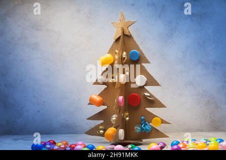 Weihnachtsbaum aus Pappe, verziert mit recycelten Materialien auf abstraktem Hintergrund Stockfoto