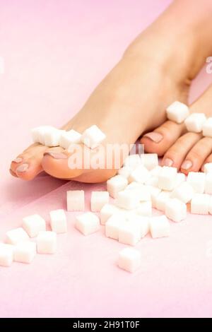 Zuckerwürfel liegen in einer Reihe auf weiblichen Füßen auf rosa Hintergrund mit Kopierraum, Enthaarungskonzept Stockfoto