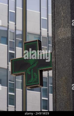 Offenes Apothekengeschäft, beleuchtetes Schild. Außenansicht des italienischen Pharmageschäft mit beleuchtetem grünen Kreuz in Mailand. Stockfoto