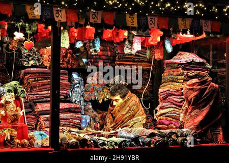 EDINBURGH, SCHOTTLAND - 18. DEZEMBER 2019: Stallangestellter auf dem Edinburgh Christmas Market huddelt in einigen der Schals, die sie verkaufen, um Wärme. Stockfoto