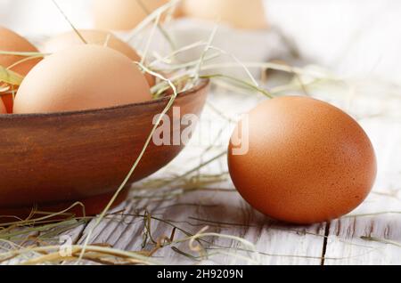 Raw organic braunen Hühnereier in Ton Schüssel auf weiße Küche Holztisch Stockfoto