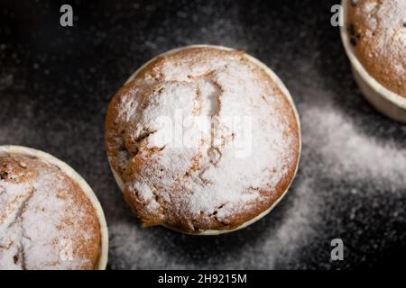 Frisch gebackene Muffins mit Schokolade und Rosinen. Auf einem Backblech verteilen. Einige werden mit Puderzucker bestreut. Nahaufnahme. Stockfoto