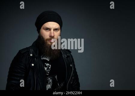 Porträt eines hübschen bärtigen Mannes in Lederjacke und Hut, der die Kamera anschaut. Stockfoto