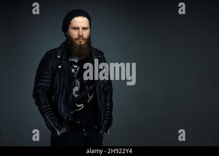 Porträt eines hübschen bärtigen Mannes in Lederjacke und Hut, der die Kamera anschaut. Stockfoto