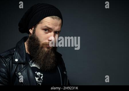 Porträt eines hübschen bärtigen Mannes in Lederjacke und Hut, der die Kamera anschaut. Stockfoto