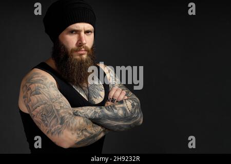 Porträt eines hübschen bärtigen Mannes in einem schwarzen T-Shirt und Hut, der auf die Kamera schaut. Stockfoto