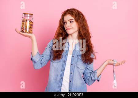 Foto von süßen unsicher junge Dame gekleidet Jeans Hemd Wahl Macaroni oder Diät isoliert rosa Farbe Hintergrund Stockfoto