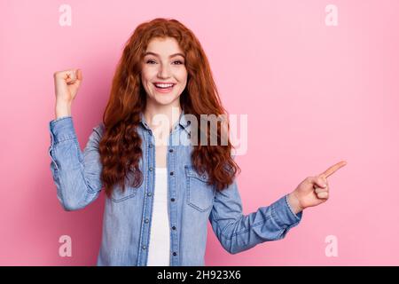 Foto von niedlichen glücklichen jungen Dame gekleidet Jeans lächelnd steigende Faust zeigen Finger leeren Raum isoliert rosa Farbe Hintergrund Stockfoto