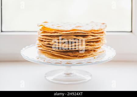 Gebackene Krümel Kuchen aus Blätterteig für die Schicht Kuchen auf einem Glasständer auf Fensterbank. Halbzeug für Kuchen. Nahaufnahme, selektiver Fokus, Sha Stockfoto