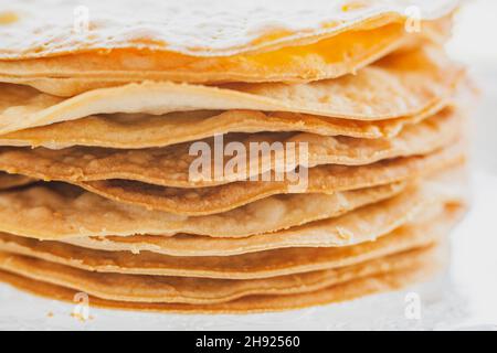 Gebackene Krümel Kuchen aus Blätterteig für Schichtkuchen auf einem Glasständer. Halbzeug für Kuchen. Nahaufnahme, selektiver Fokus, geringe Tiefe von Stockfoto