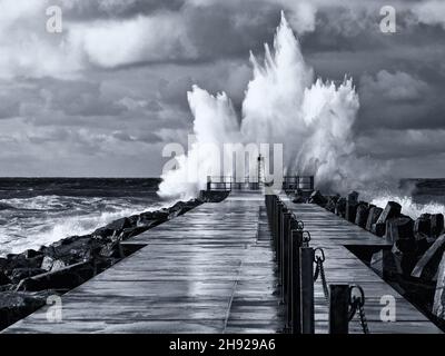 Schwarz-Weiß-Foto des Leuchtturms am Pier von Norre Vorupor bei Sturm und hohen Wellen, Jütland, Dänemark Stockfoto