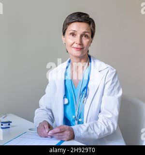 Lächelnde Ärztin mittleren Alters, die am Arbeitsplatz auf die Kamera schaut Stockfoto