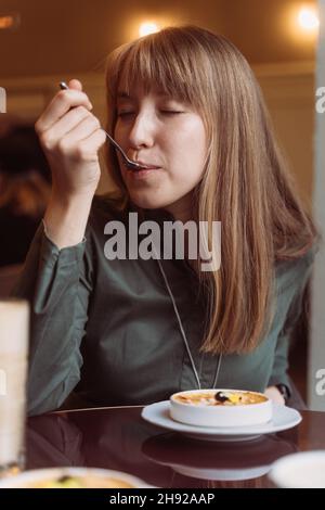 Junge Hündin, die in einem Café das Nachtisch mit Rahm Brulee genießt. Probieren Sie köstliche karamellisierte catalonia Crema Stockfoto