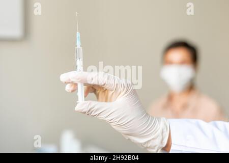 Anonyme Gesundheitsarbeiterin, die eine Patientin mittleren Alters impft. Unscharfer Hintergrund Stockfoto