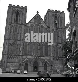 1965, historisch, das Äußere der Kathedrale von Ripon, Yorkshire, England, Großbritannien. Autos aus der Zeit parkten draußen, darunter ein Comer-Van. Die Cathedral Church of St Peter and St Wilfird, um ihr ihren vollständigen Namen zu geben, war bis 1836 als Ripon Minster bekannt und hat eine Krypta, die von Saint Wilfird erbaut wurde und England um 255 Jahre vordatiert. In diesem Jahr erreichte das Münster den Status einer Kathedrale und Ripon wurde eine Stadt. Stockfoto