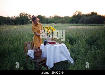 Garten und Stillleben. Teeparty im Garten - Mädchen und Strauß mit Sonnenblumen auf dem Tisch Stockfoto
