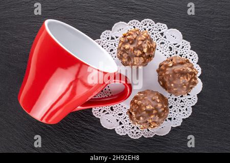 Drei süße Pralinen mit Nüssen mit einer Keramikschale auf einem Schieferstein, Nahaufnahme, Draufsicht. Stockfoto