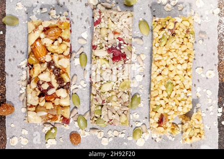 Verschiedene Müsliriegel mit Nüssen, Samen, Hafer, Beeren und trockenen Früchten auf weißem Pergament-Papier. Protein-Müsliriegel. Granola superfoo Stockfoto