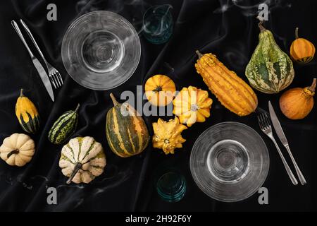 Der Tisch ist mit einer schwarzen halloween Tischdecke mit Kürbissen und einem Set Teller und Besteck bedeckt Stockfoto