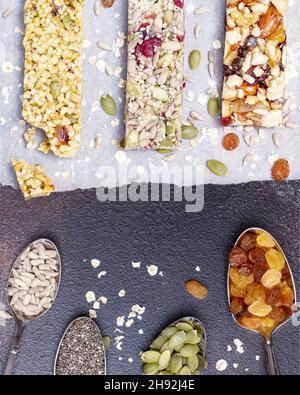 Verschiedene Müsliriegel mit Nüssen, Samen, Hafer, Beeren, trockenen Früchten und Löffeln mit Zutaten auf dunkelbraunem Hintergrund. Protein mues Stockfoto