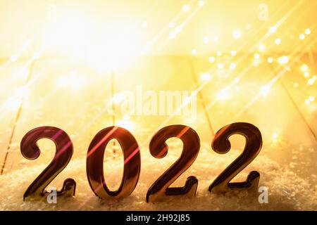 Goldzahlen 2022 auf gelbem Hintergrund mit anamorphem Filter und leuchtender Girlande. Neujahr im Hintergrund mit 2022 Jahren Stockfoto