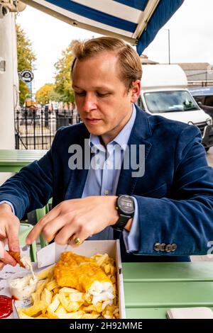 Ein gut gekleideter junger Mann, der eine Fish and Chip-Mahlzeit isst, London, Großbritannien. Stockfoto