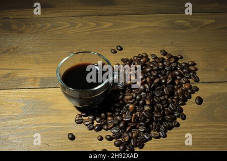 Nahaufnahme einer Tasse Kaffee und einem Stapel Kaffeebohnen, die auf einem Holztisch isoliert sind Stockfoto