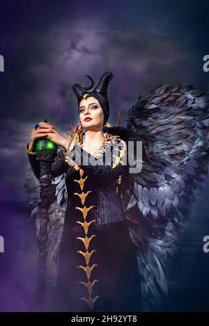 MALEFICENT COSPLAY. PORTRÄT, DUNKLER CHARAKTER MIT SCHARFEN HÖRNERN UND STARKEN FLÜGELN. BÖSE FEE IN SCHWARZEM KLEID. GELBE AUGEN. VERTIKAL. KALTE FARBEN. Stockfoto