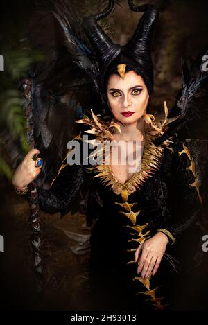 MALEFICENT COSPLAY. PORTRÄT, DUNKLER CHARAKTER MIT SCHARFEN HÖRNERN UND STARKEN FLÜGELN. BÖSE FEE IN SCHWARZEM KLEID. GELBE AUGEN. VERTIKAL. FARBE. Stockfoto