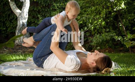Fröhliches, fröhliches Baby mit Mutter, die im Park auf Gras spielt. Elternschaft, Familie, Kinderentwicklung und Spaß in der Natur. Stockfoto