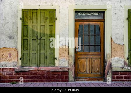 Alte, verwitterte Hausfassade mit geschlossenen Fensterläden und Eingang zu einem lange leerstehenden Einzelhandelsgeschäft für Kolonialwaren Stockfoto