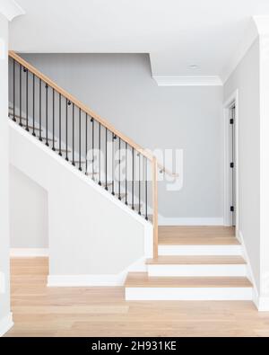 Eine Treppe mit Stufen und Handläufen aus natürlichem Holz, weißen Steigleitungen und schmiedeeisernen Spindeln. Stockfoto