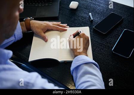 Overhead-Ansicht eines Mannes, der in einem Notizbuch mit leeren, leeren Papierblättern mit Platz für Werbetexte schreibt, Projekte plant und Notizen in einem Tagebuch macht. Schließen-U Stockfoto