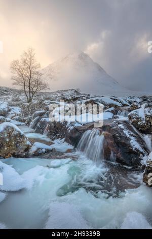 Der gefrorene Fluss Coupall fließt an einem winterlichen Tag in Glencoe, Schottland, an Stob Dearg (dem markanten Gipfel auf Buachaille Etive More) vorbei. Stockfoto