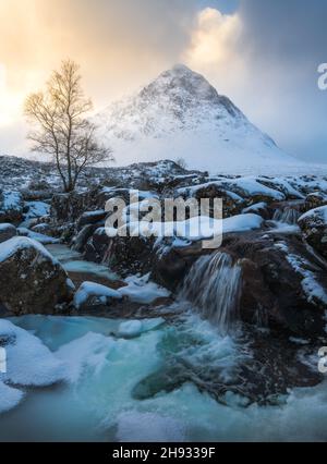 Der gefrorene Fluss Coupall fließt an einem winterlichen Tag in Glencoe, Schottland, an Stob Dearg (dem markanten Gipfel auf Buachaille Etive More) vorbei. Stockfoto